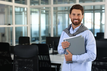 Happy man with folders in office, space for text