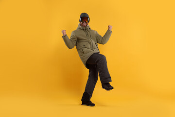 Winter sports. Cheerful man in ski suit and goggles on orange background