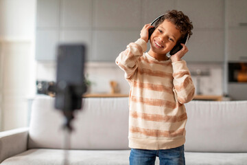 Little black boy wearing headphones and dancing in front of smartphone camera