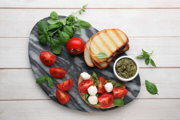 Delicious Caprese sandwich with mozzarella, tomatoes, basil and pesto sauce on white wooden table, top view