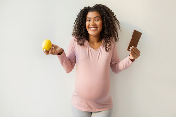 Pregnancy Cravings. Black pregnant woman holding apple and bar of chocolate