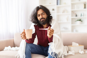 Unhealthy hindu guy checking body temperature, home interior