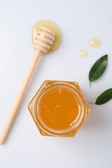 Tasty honey in glass jar, dipper and leaves isolated on white, top view