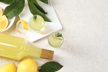 Tasty limoncello liqueur, lemons and green leaves on light textured table, flat lay. Space for text
