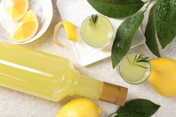 Tasty limoncello liqueur, lemons and green leaves on light textured table, flat lay