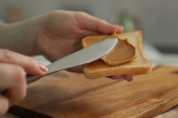 Woman spreading tasty nut butter onto toast at table, closeup