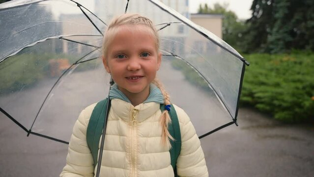 Little European girl schoolgirl standing street city outside umbrella rainy weather autumn learner education child smiling kid daughter looking at camera pupil lessons recreation funny back to school