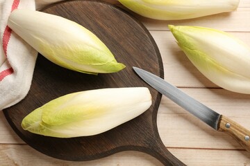 Raw ripe chicories and knife on wooden table, top view