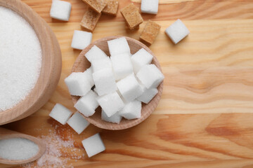 Bowls and scoop with different types of sugar on wooden table, flat lay. Space for text