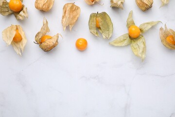 Ripe physalis fruits with calyxes on white marble table, flat lay. Space for text
