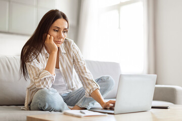 Upset Young Woman Looking At Laptop Screen While Working At Home Office