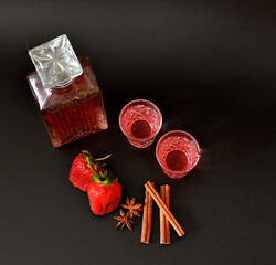 Strawberry liqueur with spices, strong homemade alcohol in a crystal decanter and two glasses on a...