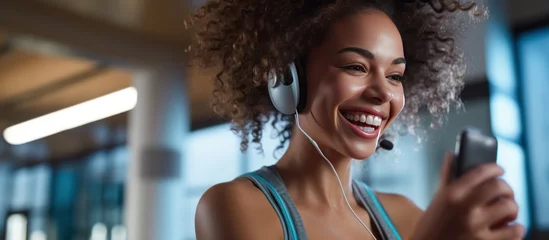 Fototapete Happy athletic woman listens music over earbuds while using cell phone in gym. © caucul