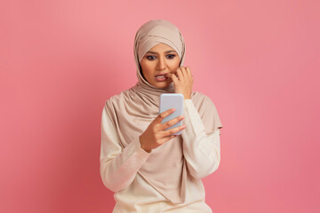 Shocked arab muslim woman in hijab looking at smartphone and biting nails