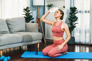 Athletic and sporty woman sitting, resting on fitness mat after finishing home body workout exercise session for fit physique and healthy sport lifestyle at home. Gaiety home exercise workout training