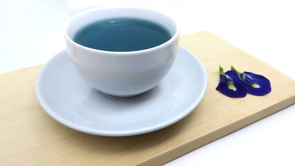 Butterfly pea tea or blue pea drink, white cup and wooden board, with butterfly pea flowers, isolated on white background. herbal or tea background