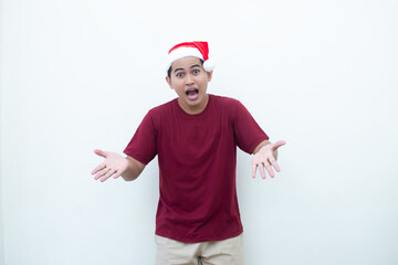 Young Asian man wearing a Santa Claus hat smiling, shock and pointing to her side isolated by white background for visual communication