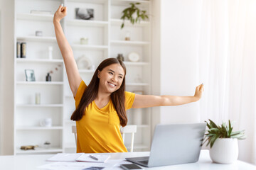 Smiling asian female freelancer stretching after working day at home office