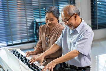 Asian senior elderly couple play piano together in living room at home.