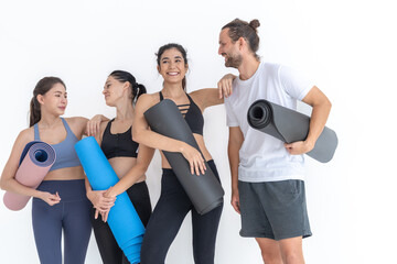 Obraz premium Group of happy sporty women talking with body stylish sportswear holding personal carpets leaned on a white background. waiting for yoga class or body weight class. healthy lifestyle and wellness