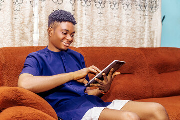 Young black man Sitting on Couch, Looking at Tablet With Engagement
