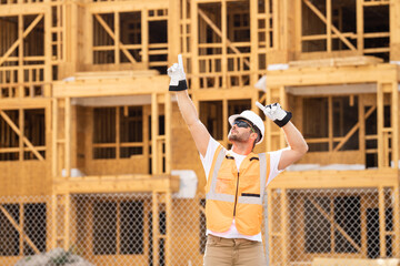 roofer builder working on roog structure of building on construction site. handsome young male builder in hard hat smiling at camera. Construction Worker on Duty. Contractor and the Wooden House Frame