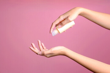 Female han pouring lotion from bottle on hand for mockup over pink background