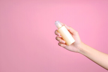 Woman hand holding plastic beige lotion bottle for mockup isolated on pink background
