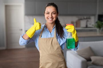 Happy housekeeper gives thumbs up with cleaning products