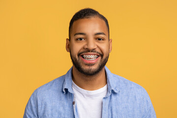 Cheerful young black man with dental braces posing against yellow background - obrazy, fototapety, plakaty