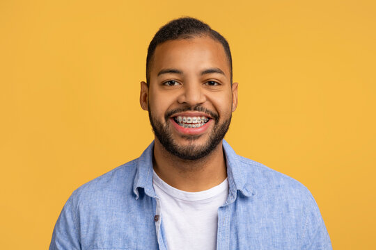 Cheerful young black man with dental braces posing against yellow background