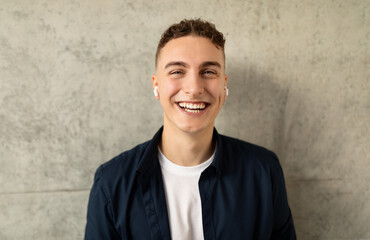 A cheerful young man with earbuds, laughing and looking at the camera