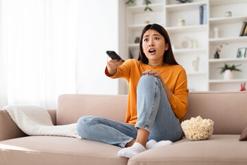 Shocked millennial asian woman watching TV at home