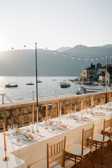 Long festive set table with candles stands on the terrace by the sea