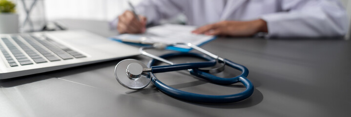 Focus stethoscope on doctor office with blurred background of doctor reviewing medical report and...