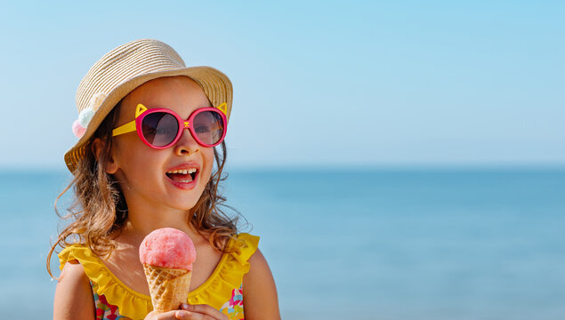 A child with an ice cream ball in a conical cup against the background of the blue sea. Enjoying a cool treat in hot weather. The child is on vacation on a trip.