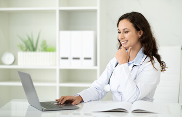 Cheerful lady in white coat has video call on laptop - obrazy, fototapety, plakaty