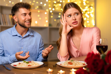 Man talking earnestly, woman annoyed at romantic dinner