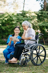 Elderly asian senior woman on wheelchair with Asian careful caregiver and encourage patient, walking in garden. with care from a caregiver and senior health insurance...