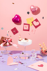 Front view of a cocktail decorated with wafer roll and chocolate. On a pastel background there are heart-shaped balloons and paper hearts. Valentine's Day theme.