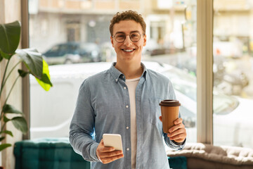 Young happy handsome european man student in glasses with coffee cup and smartphone