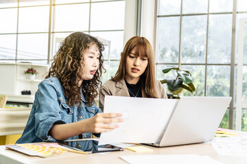 Two business young asian woman working in computer laptop together in office with reports, colleagues discuss financial data analyzing documents marketing project result talk business conversation