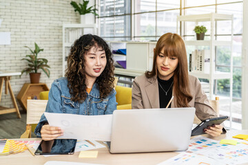 Two business young asian woman working in computer laptop together in office with reports, colleagues discuss financial data analyzing documents marketing project result talk business conversation