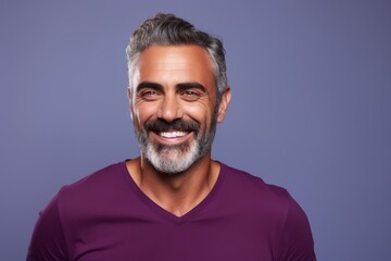 Handsome mature man in casual wear is looking at camera and smiling while standing against purple background