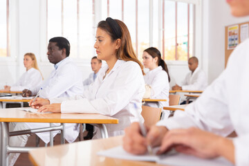 Medical students in white coats listen to a lecture in the audience
