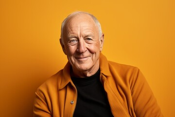 Portrait of a smiling senior man posing isolated over yellow background.