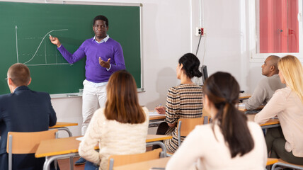 African American teacher standing near chalkboard, giving lesson to group of students as part of adult education course