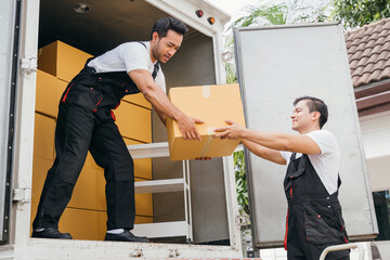 Smiling employees of a removal company work in uniform unloading boxes and furniture from the...