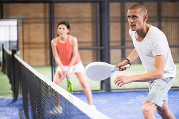 Portrait of sporty adult man playing padel on indoor court, ready to hit ball. Active lifestyle...