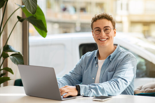 Smiling proud millennial european guy student in glasses, typing on computer